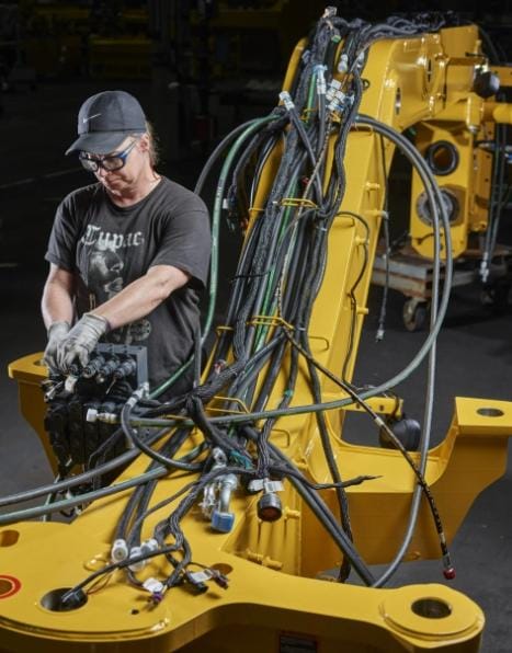 A John Deere motor grader part with hoses in a factory